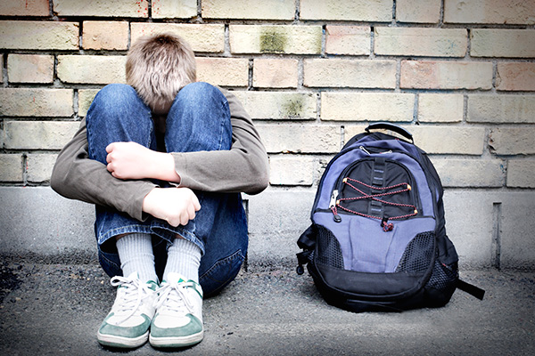 Upset boy sitting against a wall, head down against knees