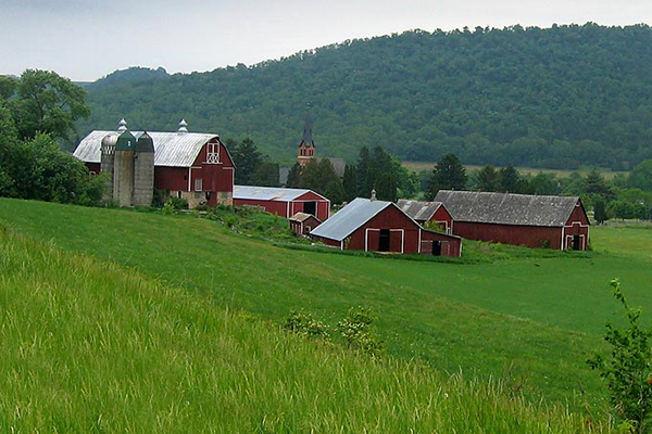 a view of a farm with red buildings and a hill behind it