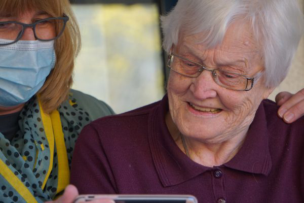 An older woman looking at a phone with a middle aged woman looking over her shoulder and assisting her