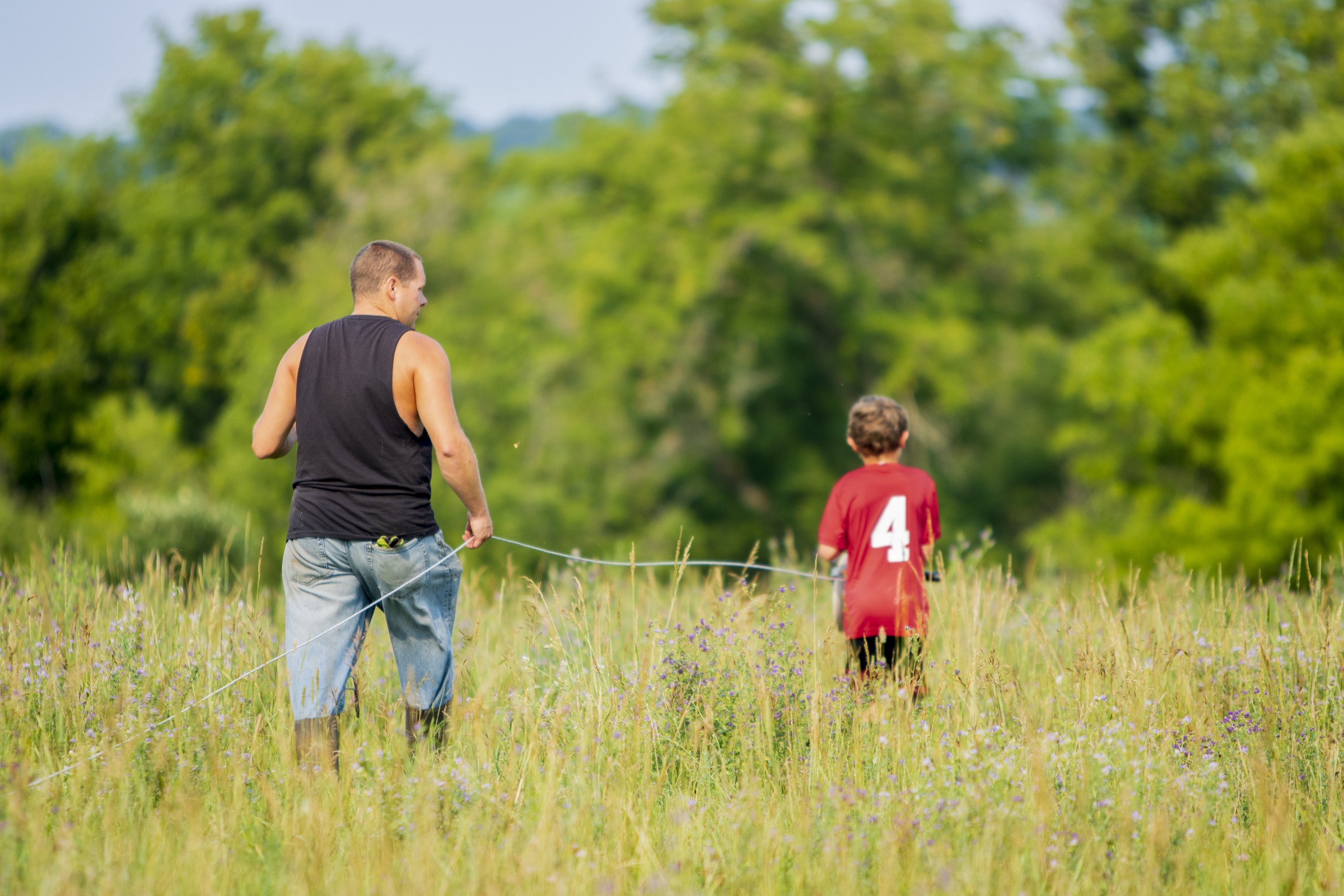 A farmer and son in a field handing up a wire fence