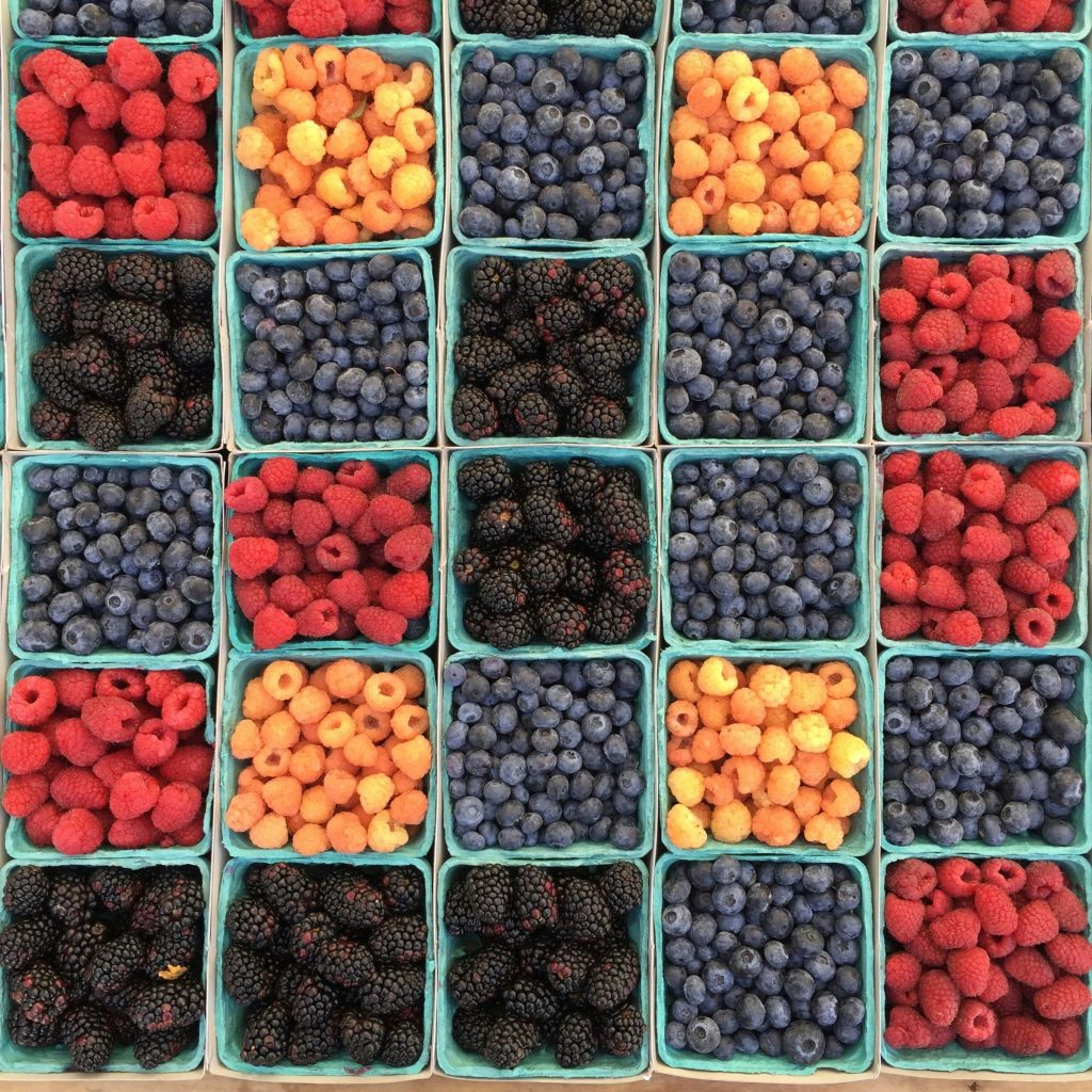 Raspberries, blueberries, and blackberries are displayed in green pint containers