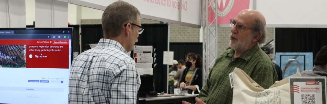 Image of a two people, one standing behind a booth talking to the other person in front of the booth