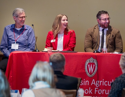 Image of three people sitting at a red table speaking on a panel
