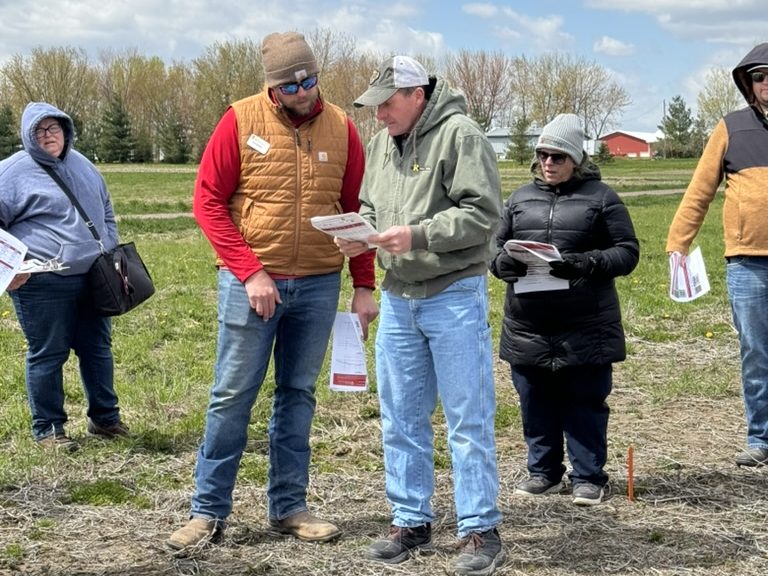 Image of two people in a field looking at a piece of paper together. 
