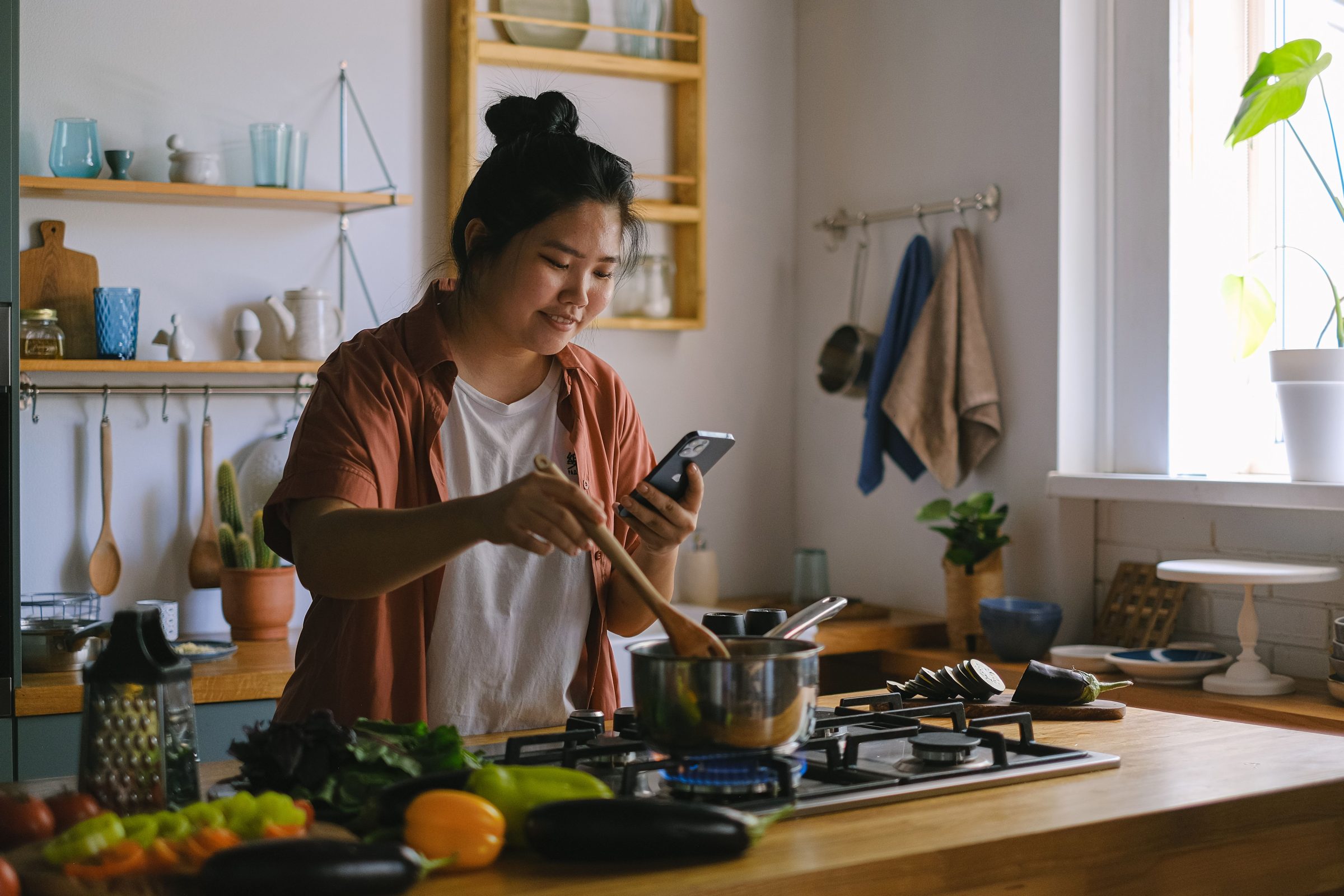 A woman cooking while looking at her phone