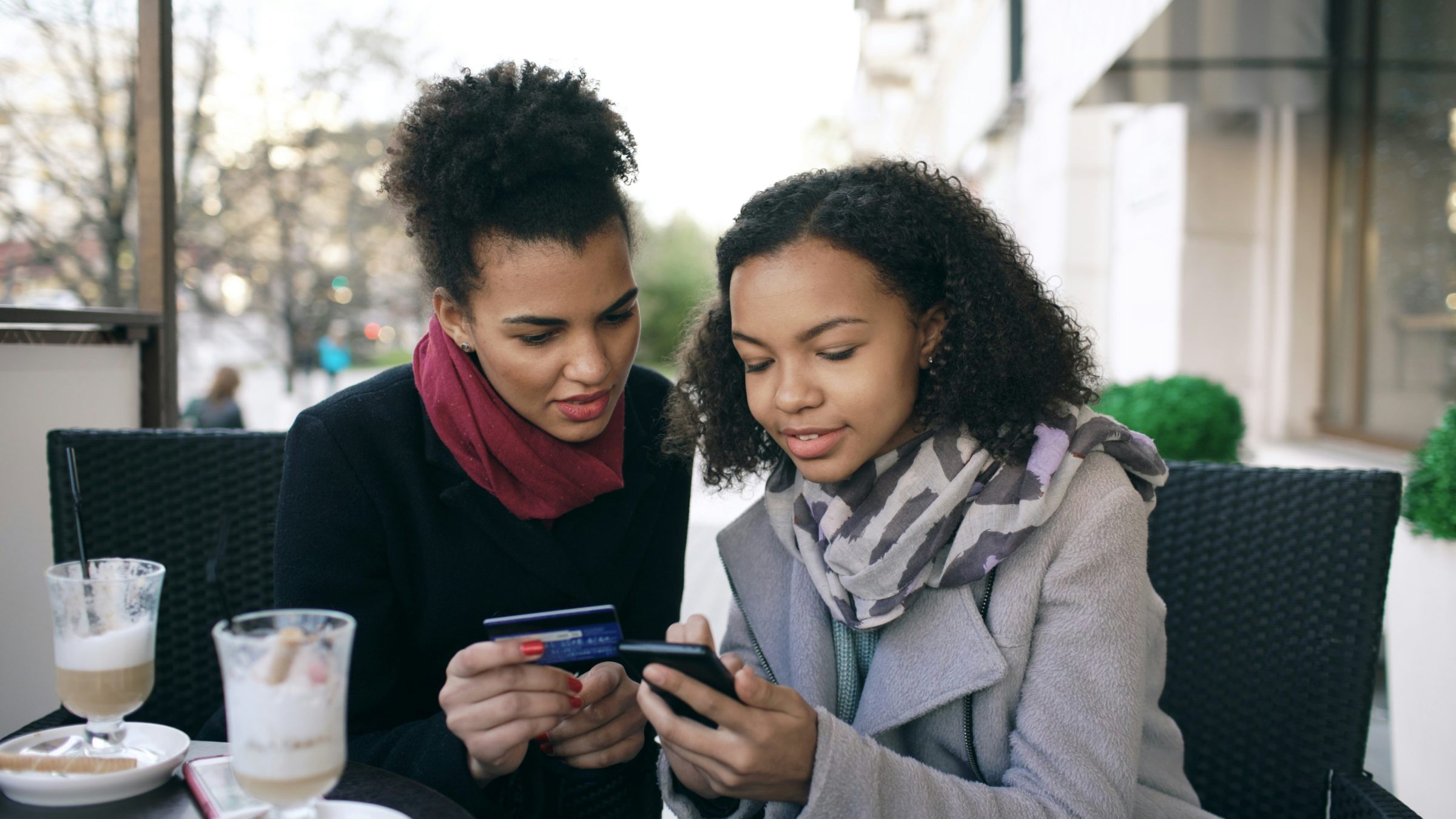 Two women discussing using a credit card while looking at a phone