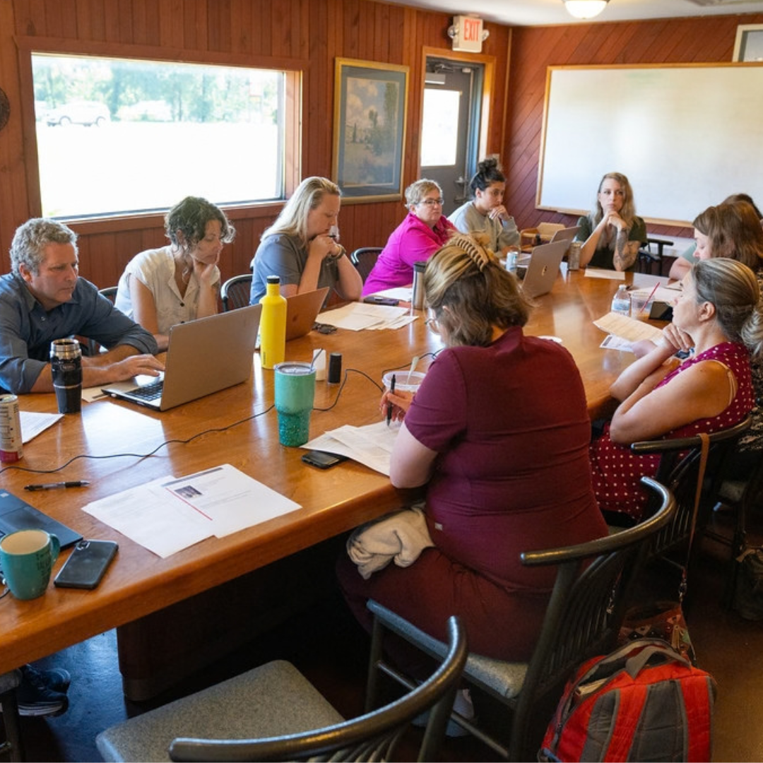 Group of people sitting around a long boardroom table discussing.