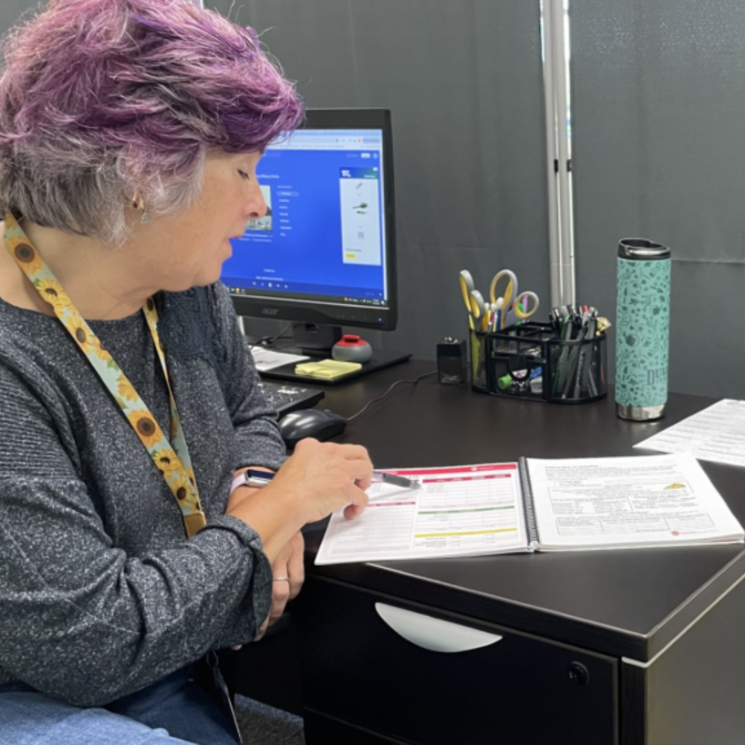 Person pointing to a workbook on a desk